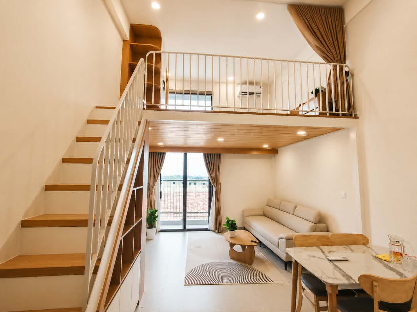 A205 — Toàn cảnh studio gác lửng với cầu thang gỗ, sofa kem và bàn ăn